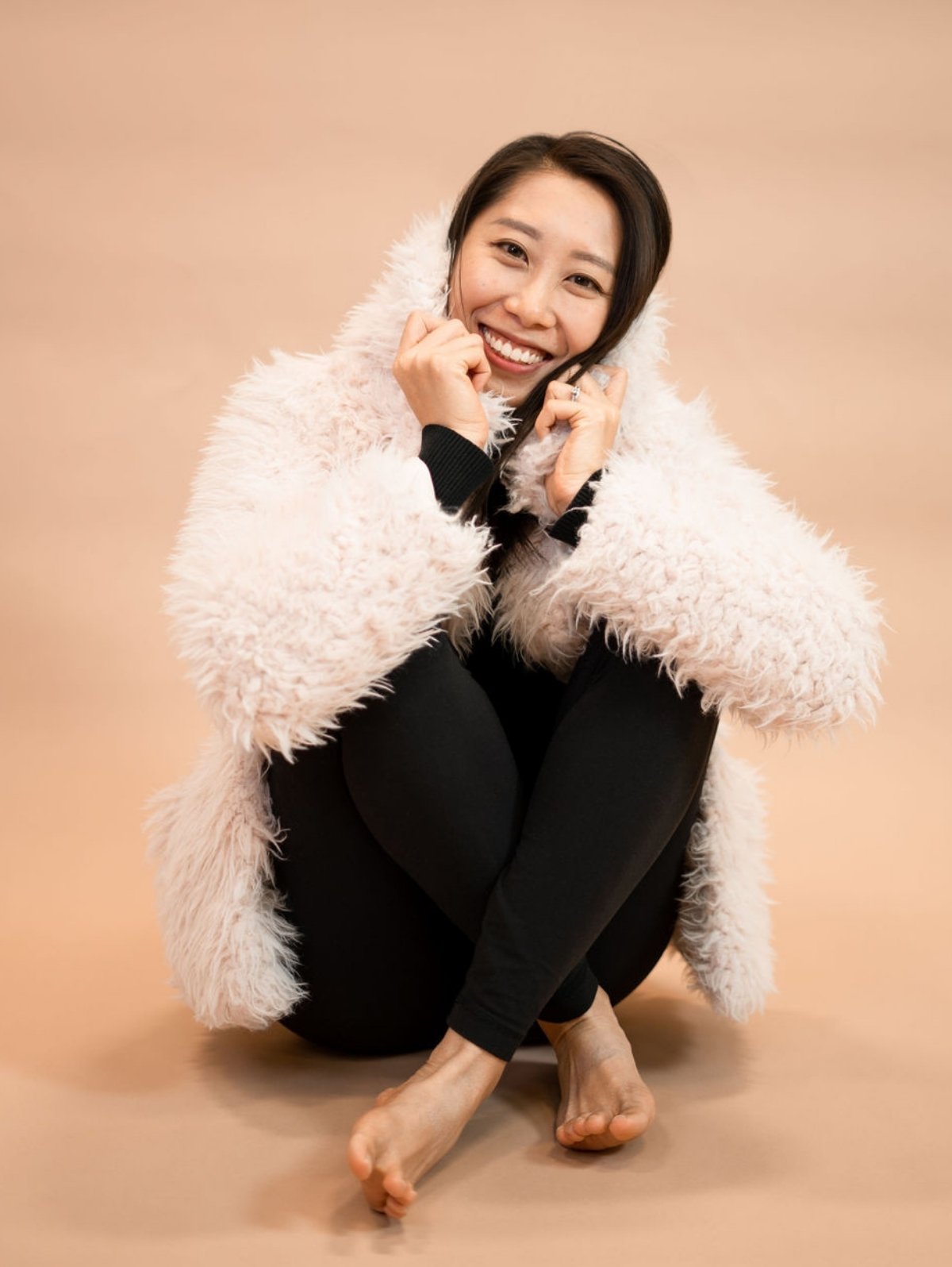 Wenwen sitting cross legged, smiling wearing the Shine your Light coat